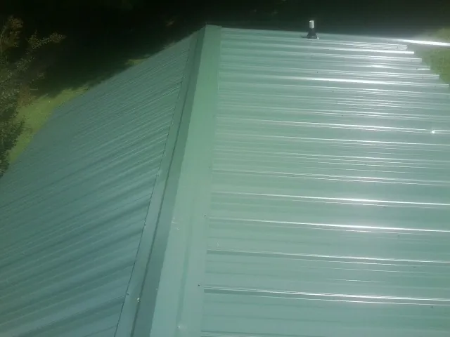 New green metal panels meeting at the ridge of a roof — Flat Roof Repair work by our crew in Sandusky